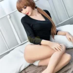 Aurélie Real Doll 165 cm IronTech Doll TPE assise sur un lit, vêtue d'un haut noir et culotte blanche.