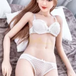 Aurélie Real Doll 165 cm IronTech en lingerie blanche allongée sur lit, cheveux longs bruns.