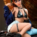 Auréline Real Doll 167 cm IronTech, assise, tenue noire sexy, oreilles pointues, lunettes sur tête.