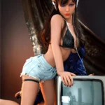 Auréline Real Doll 167 cm IronTech en bikini noir, short en jean, posant près d'une télévision rétro.