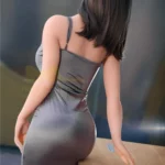 AvaDoll Sex Doll 161 cm IronTech en robe grise moulante, vue arrière appuyée sur une table.