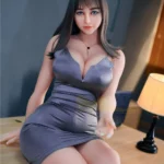 AvaDoll Sex Doll 161 cm IronTech en robe grise, assise sur une table, ambiance tamisée.