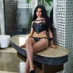 Avelina Sex Doll 168 cm en lingerie noire, assise élégamment sur un banc moderne.