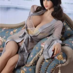 Azalée Sex Doll 163 cm en lingerie beige, posée sur un canapé fleuri, robe transparente.