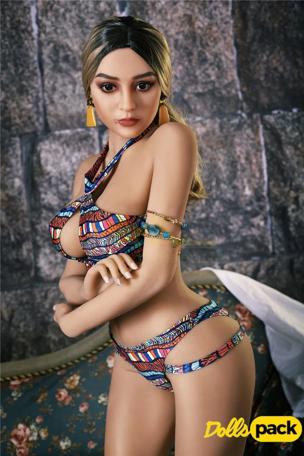 Bella Sex Doll 159 cm IronTech en bikini coloré, posée de profil sur fond de mur en pierre.