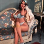 Bella Sex Doll 161 cm IronTech en lingerie grise, posée sur un canapé fleuri, ambiance élégante.
