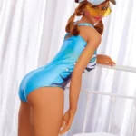 Bellara Sex Doll 153 cm IronTech en maillot bleu, casquette et lunettes, posée sur un lit.