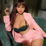 Callia Sex Doll 164 IronTech en tailleur rose, posée sur un fauteuil vert, cheveux longs.