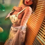 Eliya Sex Doll 163 cm IronTech en lingerie florale, pose sensuelle près de stores vénitiens.