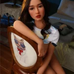 Ellea Sex Doll 166 cm IronTech Doll TPE assise sur une chaise, regard pensif, cheveux bruns.