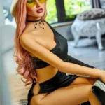 Elodora Sex Doll 165 cm IronTech en robe noire, assise, chapeau blanc, lunettes jaunes.