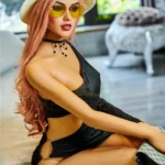 Elodora Sex Doll 165 cm IronTech en tenue noire, assise avec chapeau et lunettes jaunes.