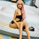 Elodora Sex Doll 165 cm IronTech, assise en robe noire, lunettes de soleil, cheveux roses.