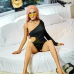 Elodora Sex Doll 165 cm IronTech Doll TPE assise sur lit, robe noire asymétrique, cheveux roses.