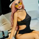 Elodora Sex Doll 165 cm IronTech TPE en robe noire, chapeau blanc et lunettes jaunes, posée sur canapé.