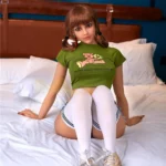 Eloiah Sex Doll 159 cm assise sur lit, T-shirt vert, chaussettes blanches, IronTech Doll.