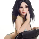 Eloïse Sex Doll 155 cm IronTech, pose assise, cheveux noirs, lingerie verte, appuyée sur un fauteuil.