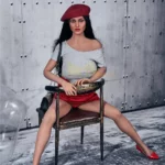 Enora Sex Doll 163 cm assise sur une chaise, portant un béret rouge et un t-shirt gris.