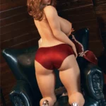 Evabella Sex Doll 158 cm posée à genoux sur un fauteuil, portant des sous-vêtements rouges.