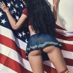 Evalia Sex Doll 163 cm en jupe bleue, pose de dos contre un drapeau américain.