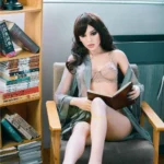 Feena Sex Doll 165 cm IronTech, assise lisant, lingerie beige, robe grise, intérieur moderne.
