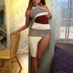 Félicine Sex Doll 164 cm en robe moulante, appuyée contre une chaise, éclairage chaleureux.