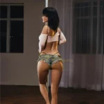 Florine Sex Doll 168 cm en short en jean, posant de dos près d'une barre de pole dance.