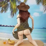 Isabelle Sex Doll 157cm IronTech en robe d'été, chapeau marron, pose à genoux sur une table de plage.