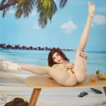 Isabelle Sex Doll 157cm IronTech allongée sur table, pose sensuelle, plage tropicale en arrière-plan.
