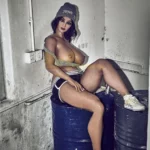 Léoline Sex Doll 158 cm IronTech en tenue décontractée, assise sur des barils dans un décor industriel.