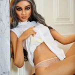 Lilouise Sex Doll 165 cm IronTech Doll TPE en lingerie beige, posée contre un mur, chemise ouverte.