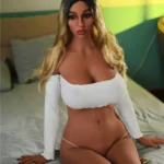 Lilouvette Sex Doll 163 cm assise sur un lit, portant un haut blanc, ambiance intime.