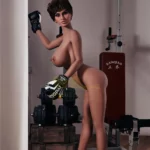 Lulabelle Sex Doll 163 cm posée debout avec gants de boxe, près d'équipements de gym.