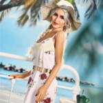 Lullia Valentina Sex Doll 165 cm en robe fleurie, pose décontractée sur fond de plage tropicale.