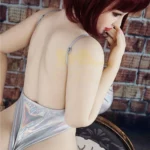 Luluca Sex Doll 158 cm IronTech, pose de profil en lingerie argentée, mur en brique.