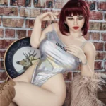 Luluca Sex Doll 158 cm IronTech Doll TPE en body argenté, assise sur chaise, fond brique.