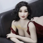 Luluva Sex Doll 160 cm IronTech allongée sur canapé noir, robe rouge, cheveux bouclés.