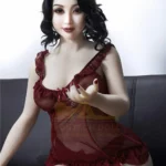 Luluva Sex Doll 160 cm IronTech en robe rouge, assise sur canapé, main tendue.