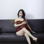 Luluva Sex Doll 160 cm IronTech Doll TPE assise sur canapé, robe rouge, pose élégante.
