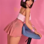 Lumabelle Sex Doll 153 cm IronTech Doll en jupe rose, pose inclinée sur tabouret bleu.