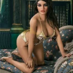 Lumelle Sex Doll 159 cm IronTech Doll TPE en lingerie dorée, posée à genoux sur un canapé fleuri.