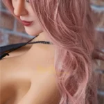 Lumielle Sex Doll 163 cm en profil, cheveux roses ondulés, lingerie noire, fond briques.