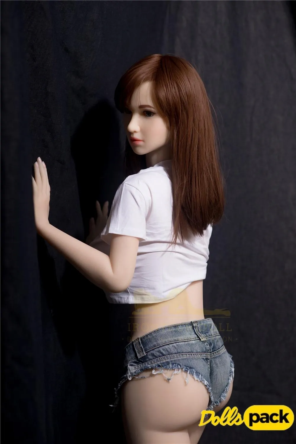 Lumiera Sex Doll 157cm IronTech Doll TPE en jean court, pose de dos contre un mur sombre.