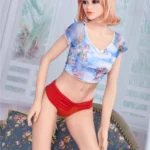 Lylia Sexy 165 cm IronTech Doll TPE posée sur canapé, cheveux blonds, haut imprimé, culotte rouge.