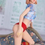 Lylia Sexy 165 cm IronTech Doll en pose à genoux, vêtue de rouge et bleu, sur canapé fleuri.
