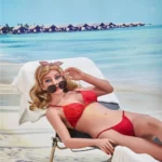 Marabelle Sex Doll 163 cm IronTech en bikini rouge allongée sur une chaise longue, plage en arrière-plan.