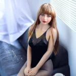 Mirabella Sex Doll 163 cm IronTech Doll TPE assise sur canapé, robe noire, cheveux longs.