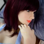 Mirabelle Sex Doll 160 cm IronTech Doll allongée, cheveux auburn, robe à carreaux bleus.