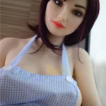 Mirabelle Sex Doll 160 cm en robe à carreaux bleus, pose assise, cheveux bruns.