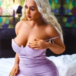 Nimaya Sex Doll 156 cm IronTech en robe mauve, assise sur un lit, cheveux blonds ondulés.